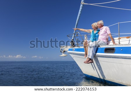 A happy senior couple sitting on the side of a sail boat on a calm blue sea looking and pointing to a clear horizon