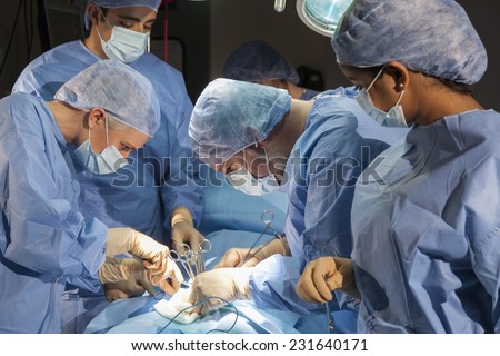 A team of interracial medical doctors male & female surgeons in surgery operating on a patient using different medical equipment instruments wearing scrubs and masks
