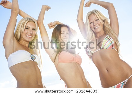 Three beautiful young women or girls in bikinis dancing backlit with sun lens flare on a sunny beach