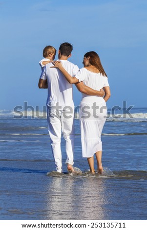 Rear view of man and woman boy child couple family in white clothes happy walking on an empty beach with bright clear blue sky