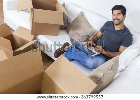 Asian Chinese Korean man packing or unpacking boxes using a laptop computer on the internet and moving into a new home.