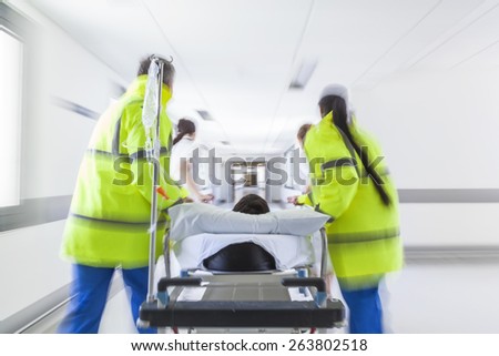 A motion blurred photograph of a patient on stretcher or gurney being pushed at speed through a hospital corridor by doctors & nurses to an accident and emergency room