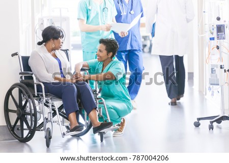 Ethnic African American female wheelchair patient with professional specialist nursing staff in corridor of hospital recovery center