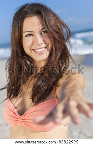 Beautiful young women or girl in bikini on a sunny beach smiling and reaching hand to the camera
