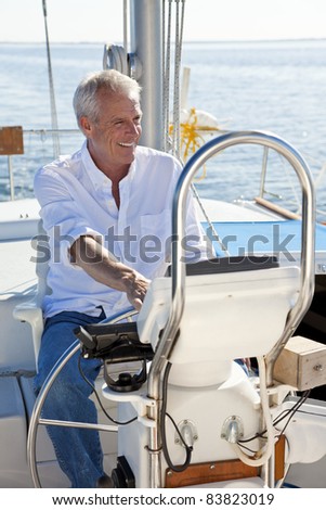 A happy senior man smiling sitting at the wheel of a sail boat on a calm blue sea