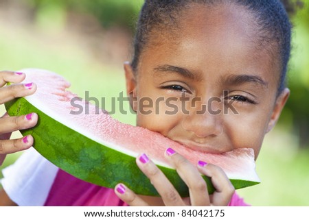 A cute, smiling & happy young African American girl child eating a slice of juicy water melon