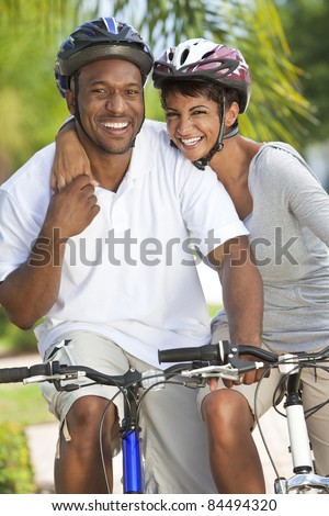 A happy laughing young African American couple with big smiles riding their bicycles outside