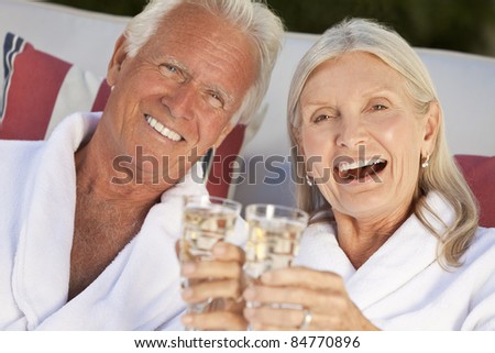 Happy senior man and woman couple at health spa in white bathrobes smiling and drinking champagne