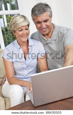 Portrait shot of an attractive, successful and happy middle aged man and woman couple in their forties, sitting together at home on a sofa using tablet computer