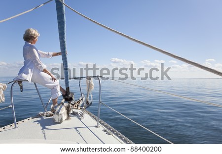 A happy senior woman sitting at the bow of a sail boat looking out to a calm blue sea