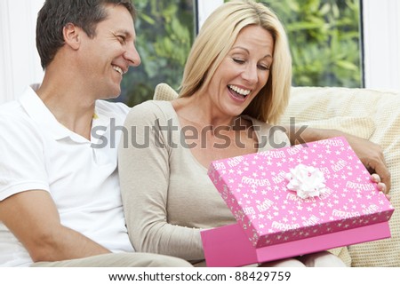 Attractive, successful and happy middle aged man and woman couple in their forties, celebrating her birthday opening a present in a pink gift box.