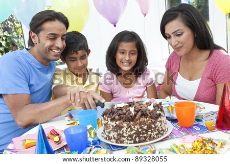 Asian Indian family, mother, father, son & daughter celebrating a birthday party cutting the cake