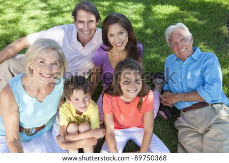 An attractive happy, smiling family of mother, father, grandparents, son and daughter sitting on the grass outside or in a garden together.