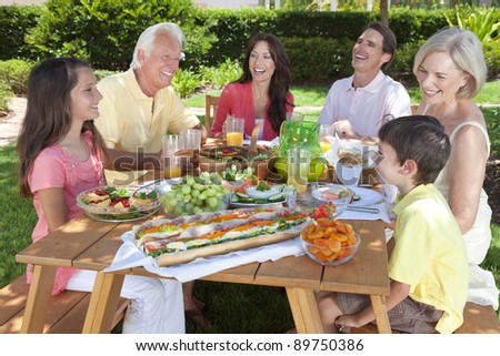 An attractive happy, smiling family of mother, father, grandparents, son and daughter eating healthy food at a picnic table outside