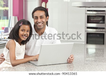 Asian Indian father and daughter, man and girl, using laptop computer in the kitchen at home