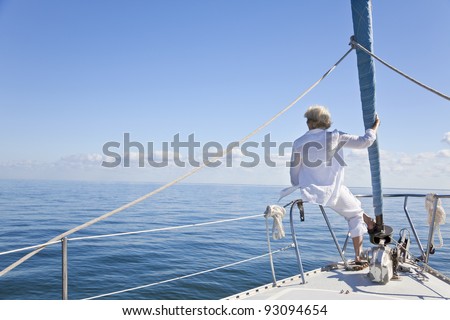 Rear view of a senior woman alone sitting on the front of a sail boat on a calm blue sea