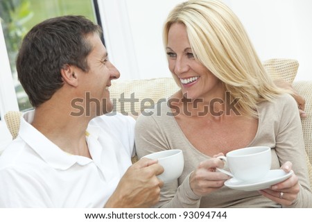 Attractive, successful and happy middle aged man and woman couple in their forties, sitting together at home on a sofa enjoying a cup or mug of tea or coffee