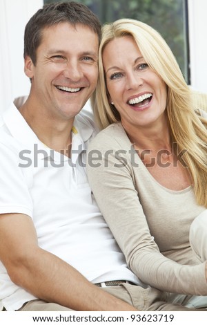 Portrait shot of an attractive, successful and happy middle aged man and woman couple in their forties, sitting together at home on a sofa, smiling and laughing