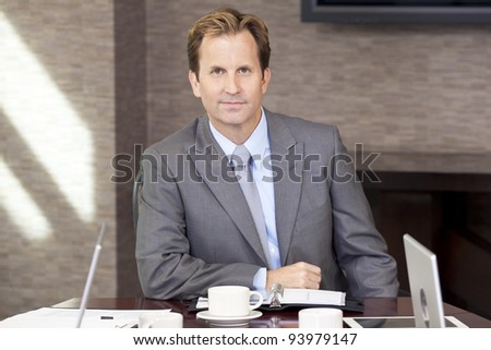 A businessman, chairman or man in a business suit, sitting at an office boardroom table