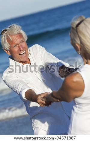 Happy senior man and woman couple dancing laughing and holding hands on a deserted tropical beach with blue sea