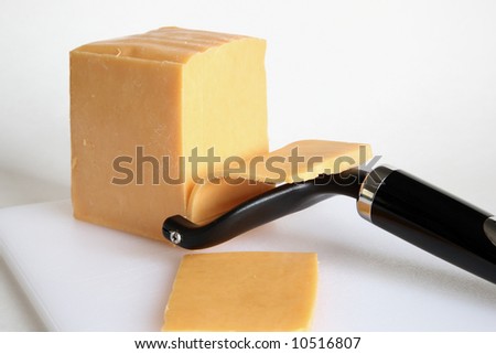 Shot of cheese slicer cutting off another slice of cheddar - close-up