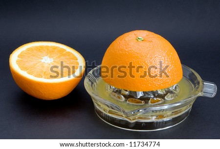 An orange juicer with cut orange. Angled top shot isolated against a black background
