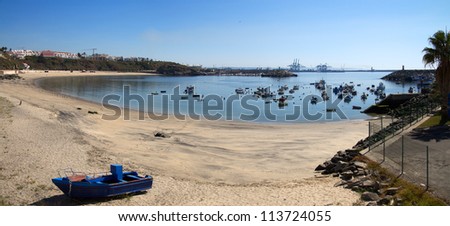 Sines beach bay and traditional fishing harbour. Industrial harbour in the horizon. Portugal.