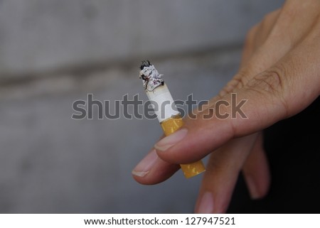 Female hand of stretched fingers holding a lighted cigar.