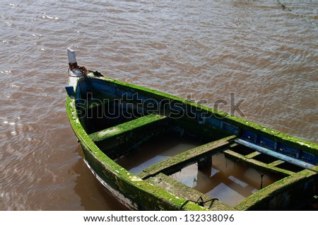 Old and abandoned wooden boat sinking on muddy water.