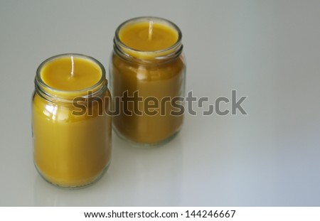 Two yellow homemade craft wax candles in glass jars.