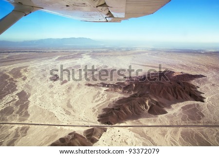 Nazca desert and panamerican highway seen from above, under the wing of a Nasca Lines airplane. Peru. Focus on the ground.