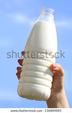 woman\'s hand with a bottle of milk on the background of blue sky