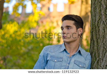 Attractive young male model outdoors in nature leaning on tree