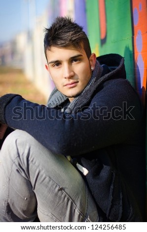 Attractive young man sitting on ground against colorful graffiti covered wall