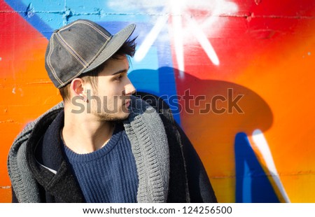 Handsome young man against colorful graffiti covered wall