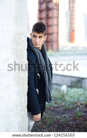 Handsome young man standing behind white wall and looking over it