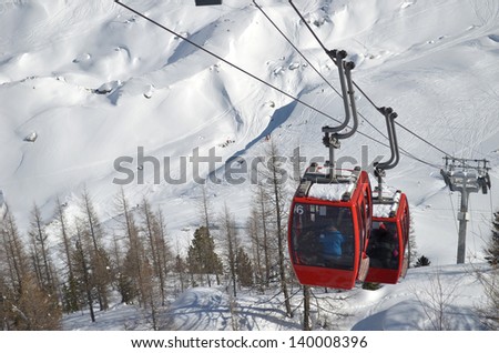 Two red cable cars climbing snow covered mountain, seen from above