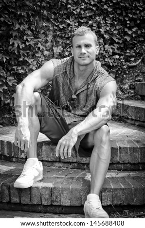 Handsome athletic young man smiling, sitting outdoors, black and white photo