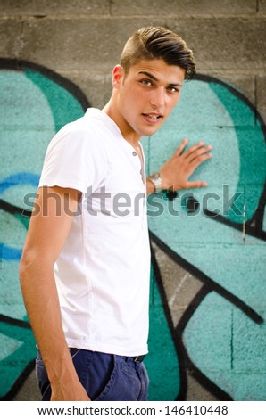 Handsome young man standing next to colorful graffiti covered wall