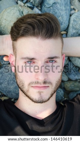 Portrait of attractive young man resting on rocks, looking in camera