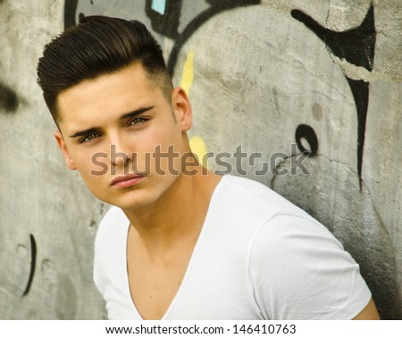 Handsome young man leaning against urban graffiti covered wall
