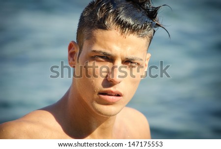Attractive young man in the sea getting out of water with wet hair, looking in camera