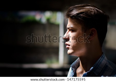 Profile of attractive young man in urban setting, lit by a ray of sunlight in the dark