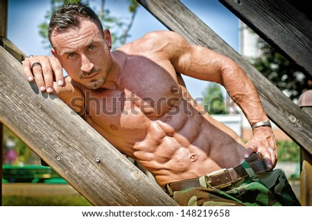 Handsome, muscular bodybuilder laying on wood stairs in the sun showing bulging pecs and abs