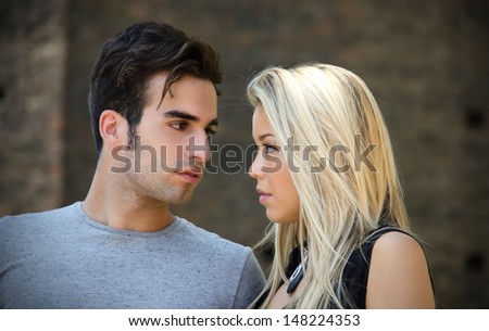 Attractive couple in love looking into each other\'s eyes, blonde girl, brown haired guy, outdoors