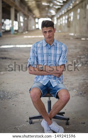 Attractive young man sitting on office chair alone in abandoned warehouse