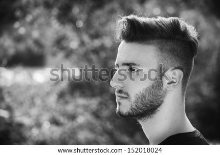 Profile portrait of handsome young man outdoors in nature, looking to a side, black and white shot