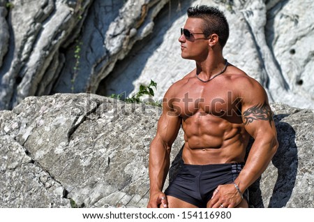 Attractive young muscle man shirtless against white rocks, looking to a side. Large copy-space