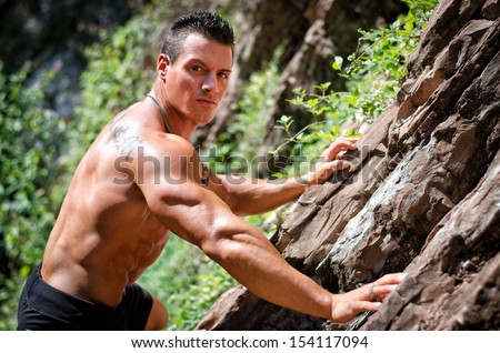 Handsome, muscular, shirless climber, looking in camera and climbing stone wall