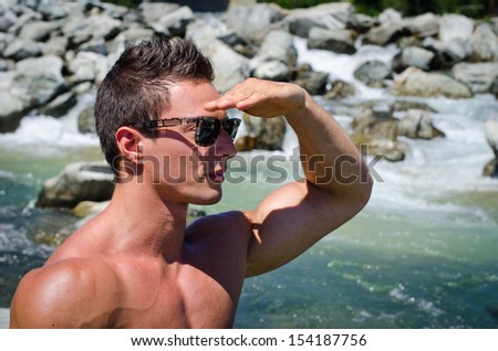 Handsome young muscular man shielding eyes with hand to look far, to a side